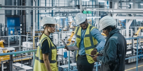 A team of factory engineers in high visibility vests working together.